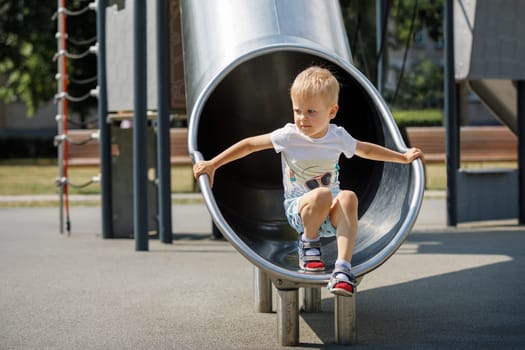 Joyful kid playing in tube slide on children's playground.