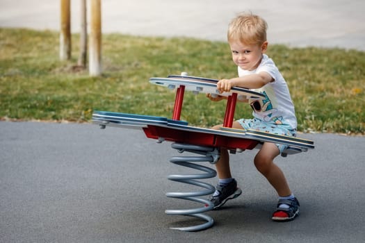 A smiling boy on a spring ground swing in a playground.