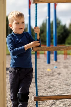 An active child in a blue sweatshirt on a playground next to a rope ladder.