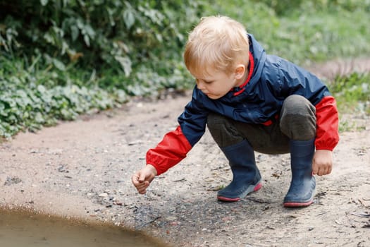 A child squat in a nature explores a dirty swamp, the little one smears his hands and face.