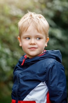 A portrait of a cheerful little, cute boy up close to nature against a green background. Vertical photo.