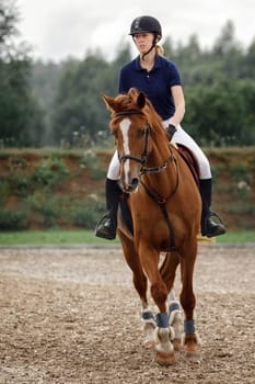 Young girl in helmet riding horse on equestrian competition.