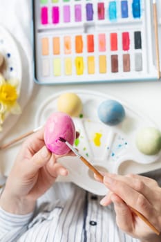 A brush in the process of painting Easter eggs with watercolors. Top view, vertical photo