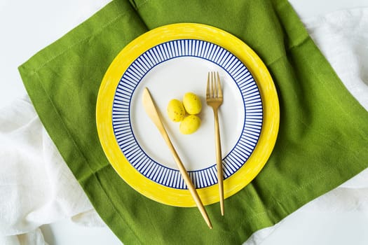 Festive table setting with bright napkins and yellow and blue plates with utensils and yellow chocolate eggs. Beautiful table design