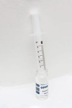 Vertical photo of Covid-19 vaccine bottle and syringe against white wall. Pharmoceutical concept.