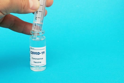 Sealed glass vial of covid-19 vaccine and syringe in the hand of a scientist or physician to observe and prepare for administration to the population.. Syringe and ampoule on blue background.