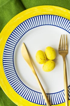 Easter serving concept. Close-up, vertical photo. Festive table setting with bright napkins and yellow-blue plates with dishes and decorated eggs