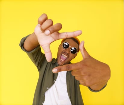 Creative young man on yellow background is seen making composition frame from his fingers, showcasing his artistic and imaginative abilities. Concept of innovation and inspiration, using hand gestures as non-verbal communication tool. High quality photo
