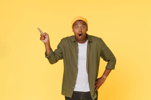 Amazed African man points to the side to copy space on yellow background. Advertising concept. High quality photo