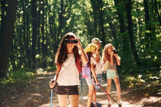Girl standing in front of her friends. Kids strolling in the forest with travel equipment.