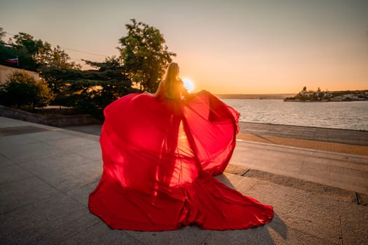 Sunrise red dress. A woman in a long red dress against the backdrop of sunrise, bright golden light of the sun's rays. The concept of femininity, harmony