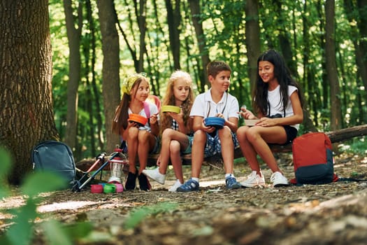 Sitting and having a rest. Kids strolling in the forest with travel equipment.