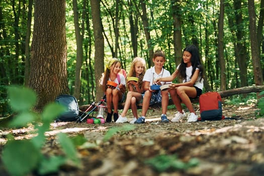 Sitting and having a rest. Kids strolling in the forest with travel equipment.