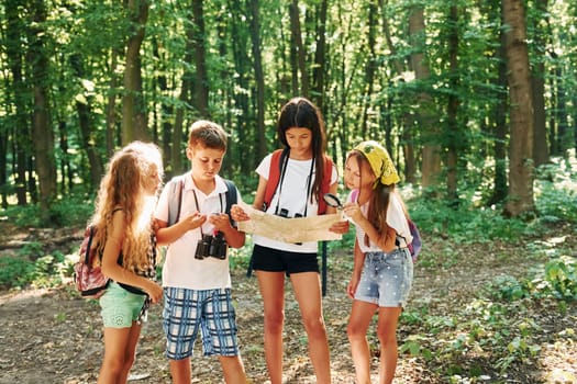 Using map to find a way. Kids strolling in the forest with travel equipment.