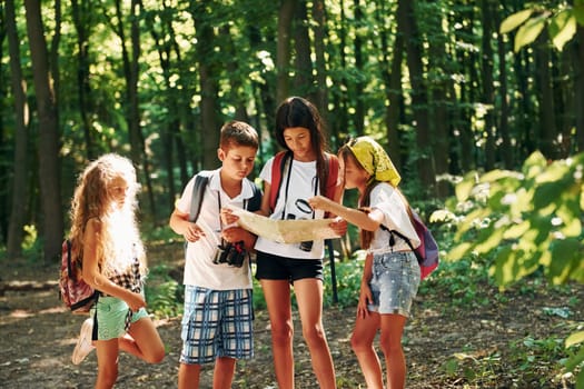 Using map to find a way. Kids strolling in the forest with travel equipment.