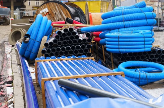 Blue and black pipelines of various diameters, concrete products and cables lie on a construction site on the street. Repair of communications.