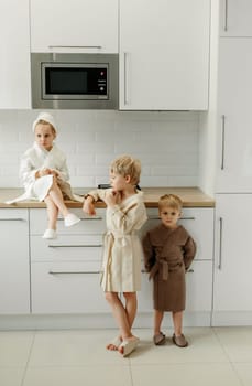 A girl and boys in bathrobes are eating marmalade in the kitchen.