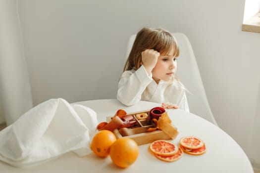 Portrait of a young girl in a dressing gown, who is sitting in the kitchen, next to a box of marmalade, candied fruits.