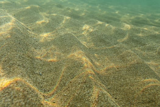 Underwater photo, sea bottom in shallow water, sun shining, light refracting on sand dunes. Abstract marine background.