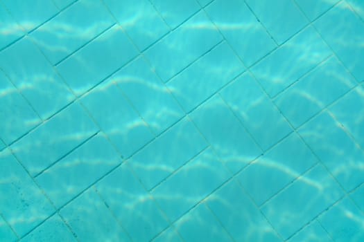 Underwater photo - old swimming pool bottom. Blue tiles pattern visible on floor. Abstract water background.