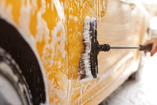 Yellow car washed at self serve carwash, detail on brush cleaning side covered in shampoo foam.