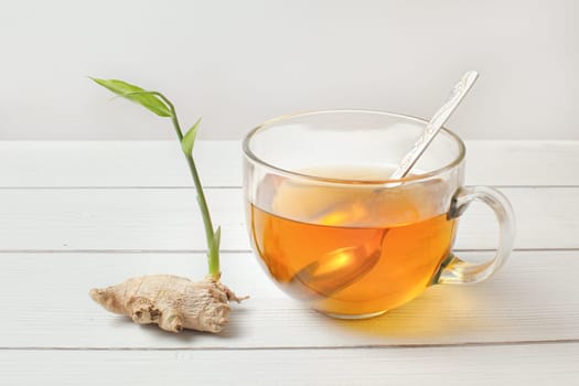 Spoon in glass cup of hot amber tea, dry ginger root with green sprout next to it.