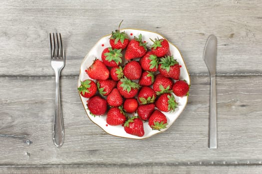 Tabletop view, plate with strawberries on gray wood boards desk, fork and knife next to it - ready to eat healthy snack concept.