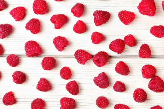 Tabletop view, raspberries spilled on white boards desk.