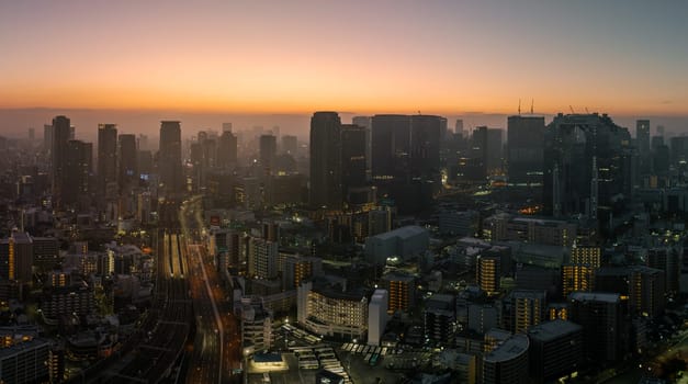 Panoramic view of Osaka Station and downtown skyscrapers before sunrise on hazy morning.