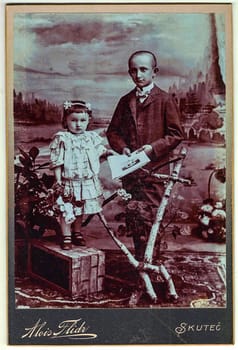 SKUTEC, AUSTRIA-HUNGARY - CIRCA, 1900: Vintage cabinet card shows children (girl and boy, siblings) posing in a photo(graphic) studio. Photo was taken in Austro-Hungarian Empire or also Austro-Hungarian Monarchy