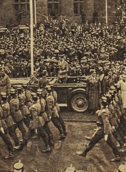 GERMANY - CIRCA 1938: Adolf Hitler waving to crowds from his car at the head of a parade. Location is unidentified. Reproduction of antique photo.