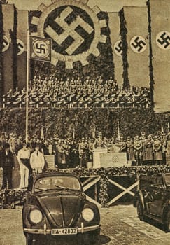 WOLFSBURG, GEMANY - MARCH 26, 1936: Wagen Germany propaganda. foundation stone laying ceremony at Fallersleben Wolfsburg Volkswagen factory with new KdF -Wagen cars on display under Nazi Swastika flags