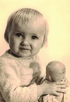 ZWICKAU, EAST GERMANY - CIRCA 1970s: The retro photo shows baby girl holds dolly. Studio photo. Black and white photo.