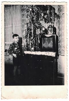 GERMANY - CIRCA 1950s: Retro photo shows social event - celebrating of Christmas Eve. Child and Christmas tree in background. Circa 1950s.