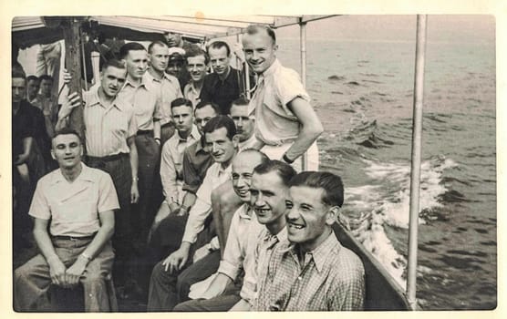 GERMANY - 1942: Vintage photo shows group of men pose on ship during a cruise. Antique black and white portrait. Circa 1940s