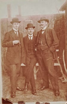 GERMANY - CIRCA 1905: Vintage cabinet card shows dandy men wear bowler hats, luxury garment and one holds cigar. Antique black and white photo. Photo with blurryd tint.
