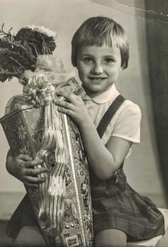 ZWICKAU, EAST GERMANY - AUGUST 30, 1969: The retro photo shows pupil girl with "Schultute" or School Cone, sweets for the first day in school. Studio photo.