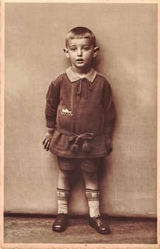 LÜNEBURG, GERMANY - CIRCA 1930s: Vintage photo shows little boy. Circa seven to eight year old. Boy wears child stockings. Studio black and white portrait. Sepia effect.