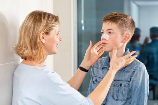 mom glues a patch to remove blackheads to her son. acne remover patch. teenage with nose band aid