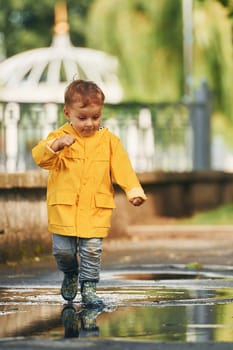 Little boy in yellow coat have a walk outdoors in the park after the rain.