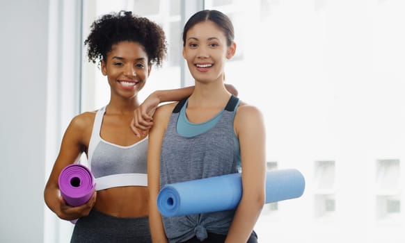 Yoga is our lifestyle. Cropped portrait of two attractive young women standing and holding yoga mats and posing before working out indoors