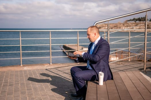 Digital Nomad, a young tattooed man working remotely online, typing on a laptop keyboard while sitting on a beach at sunset. Working remotely on vacation, running an online business from a distance