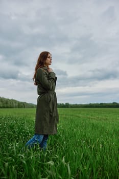 a beautiful woman in a dark coat stands in a green field in the spring in rainy weather. High quality photo