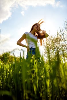 a happy woman in summer clothes stands in a field lit from behind and with her hair flying in the air. High quality photo