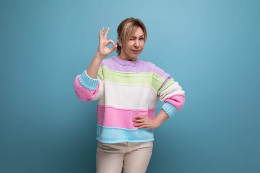 pleasant blond woman in casual outfit showing ok gesture on blue background with copy space.