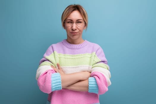 cute attractive blond woman in a striped sweater crossed her arms in front of her on a blue background with copy space.