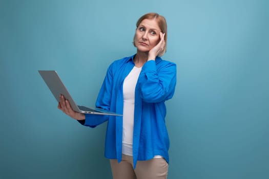 middle aged business woman working as freelancer with laptop on blue background with copy space.