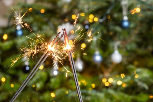 Two sparklers on the background of the Christmas tree. A couple celebrating New Year holding Bengal lights
