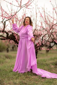 Woman peach blossom. Happy curly woman in pink dress walking in the garden of blossoming peach trees in spring.