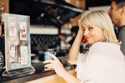 An adult mature happy couple in love in a street cafe order coffee. A blonde caucasian man and woman spend time together. Senior wife and husband walking outdoors